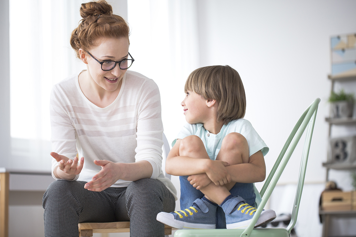 Mother talking to her smiling son sitting on green chair about school